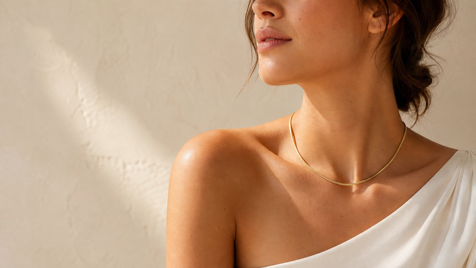 Model wearing a slim gold necklace in warm studio light