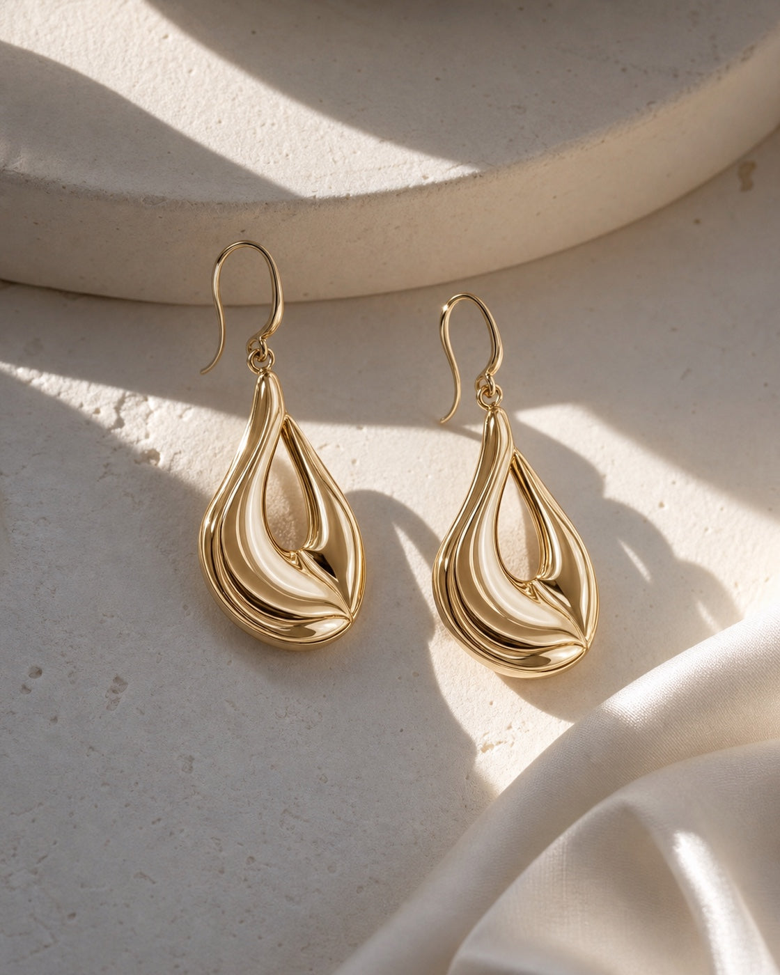 Sculptural champagne gold earrings on warm ivory stone