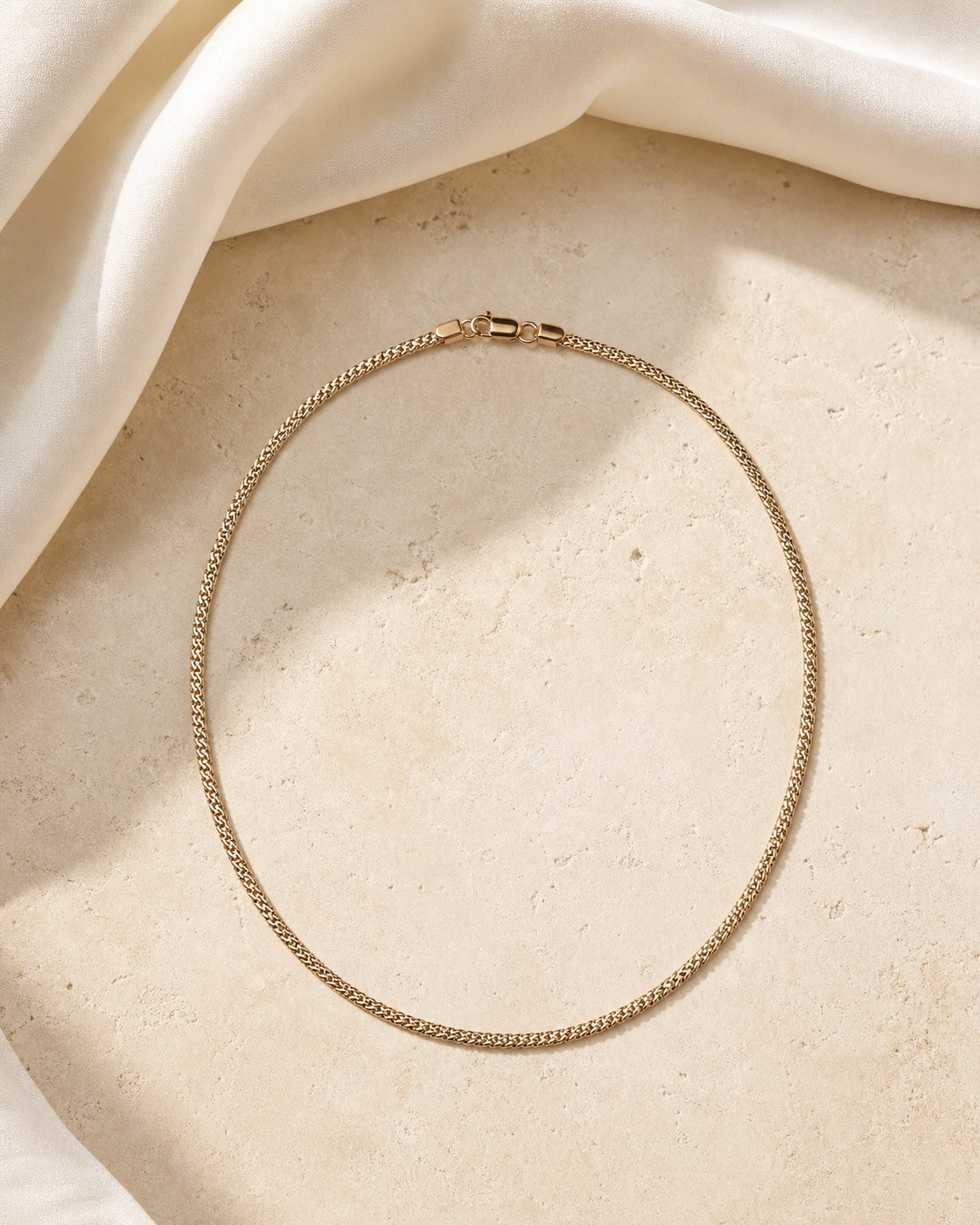 Champagne gold necklace arranged on ivory stone and silk