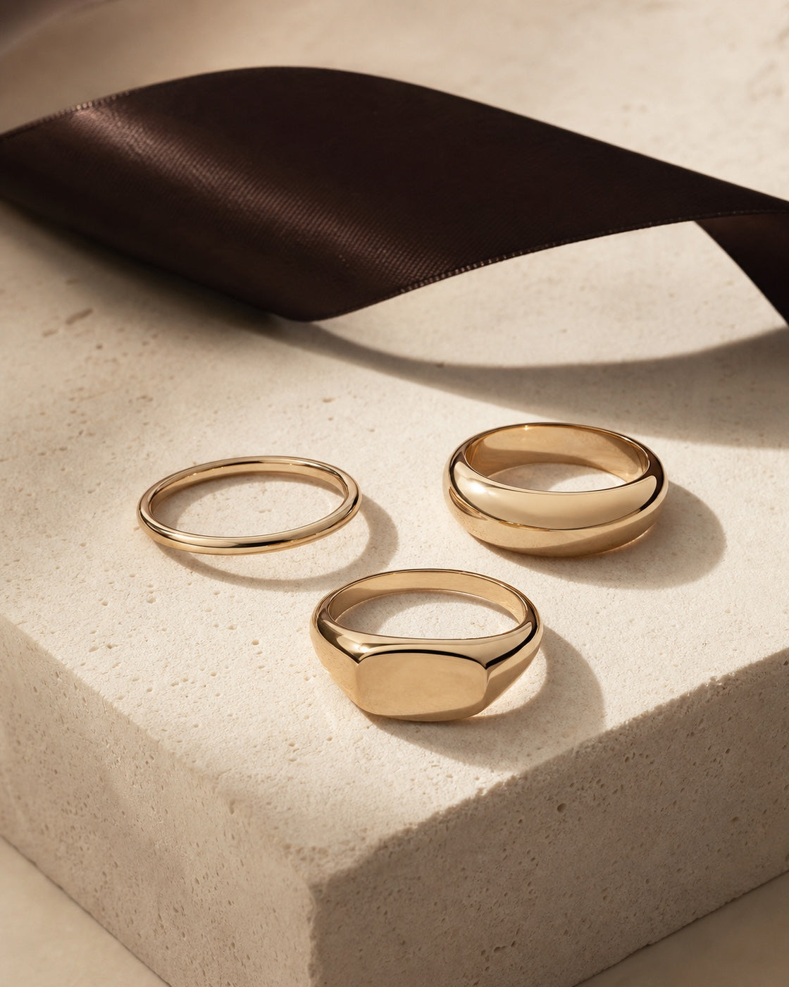 Three polished champagne gold rings on an ivory plinth